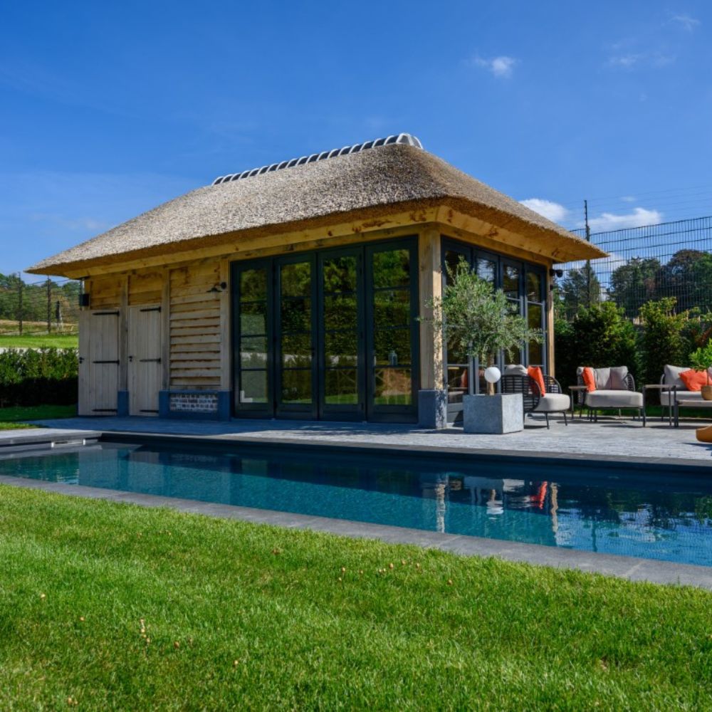 Houten poolhouse met rieten dak, glazen deuren en zwembad in de tuin