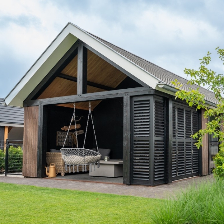 Modern houten bijgebouw met zwarte accenten, lamellen en overdekte loungehoek