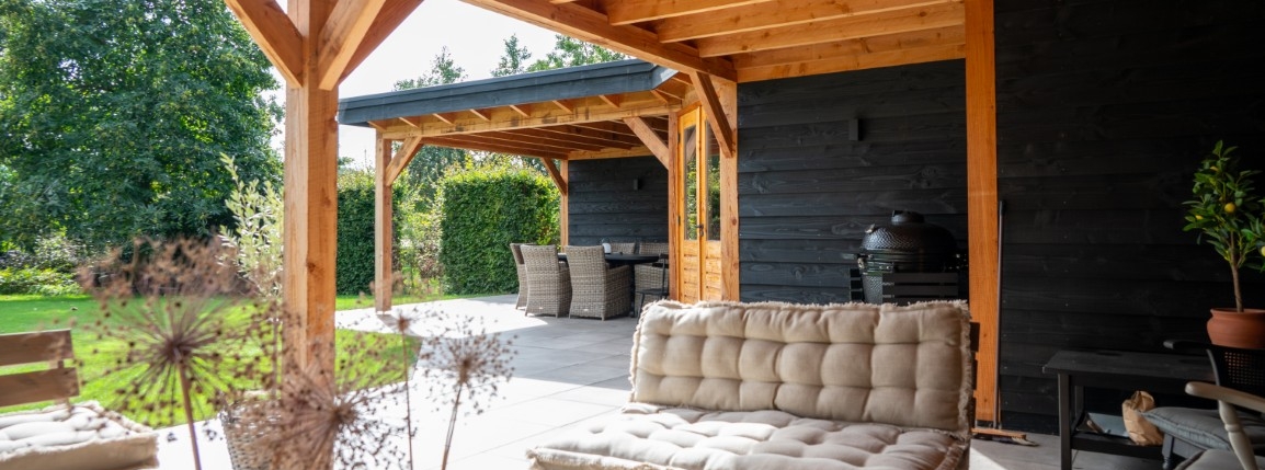 Overdekte buitenruimte met houten balkconstructie, loungehoek en buitenkeuken